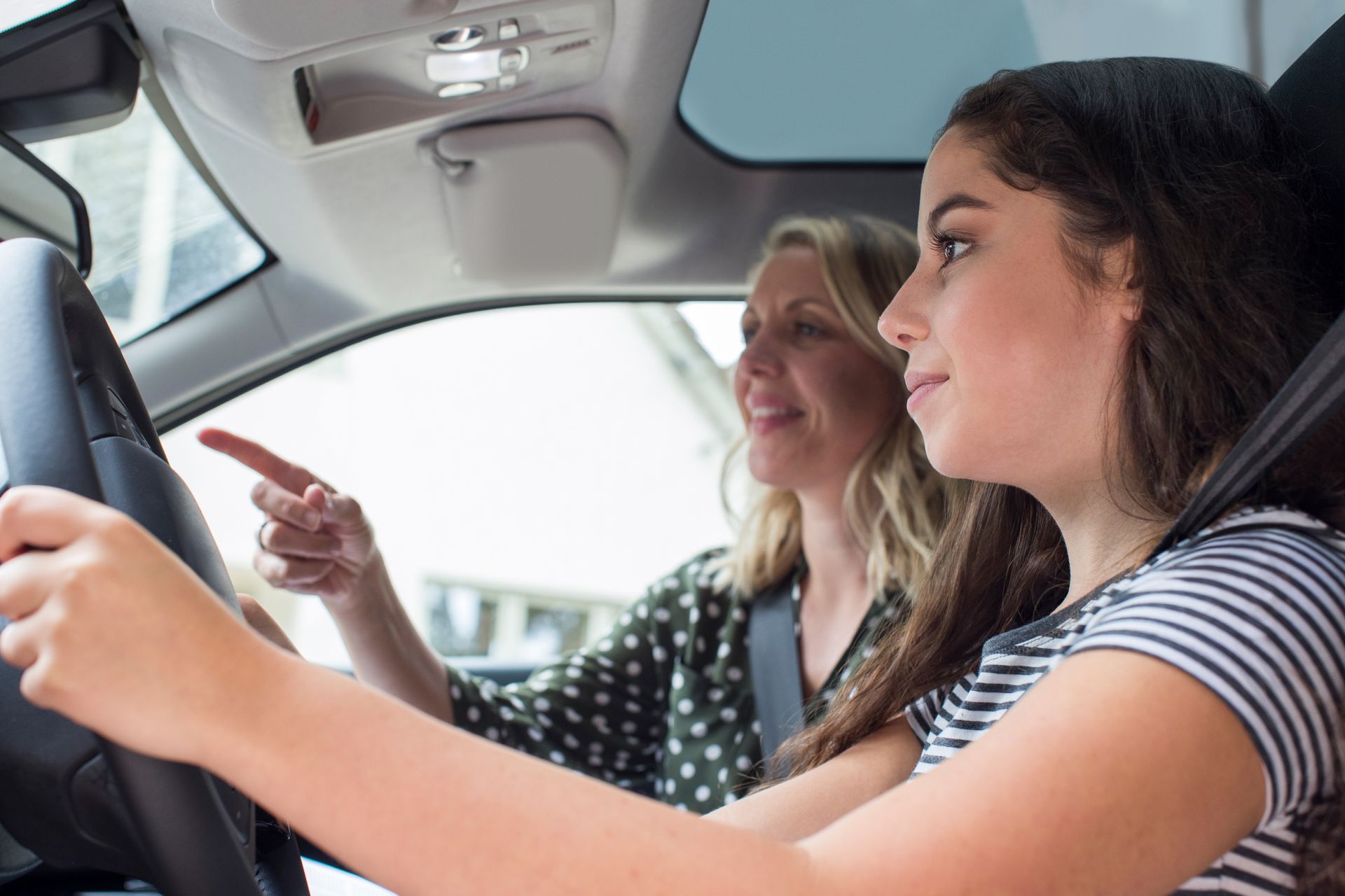 Woman guiding a young driver in a car, pointing ahead, interior view. Woman guiding a young driver in a car, pointing ahead, interior view.
