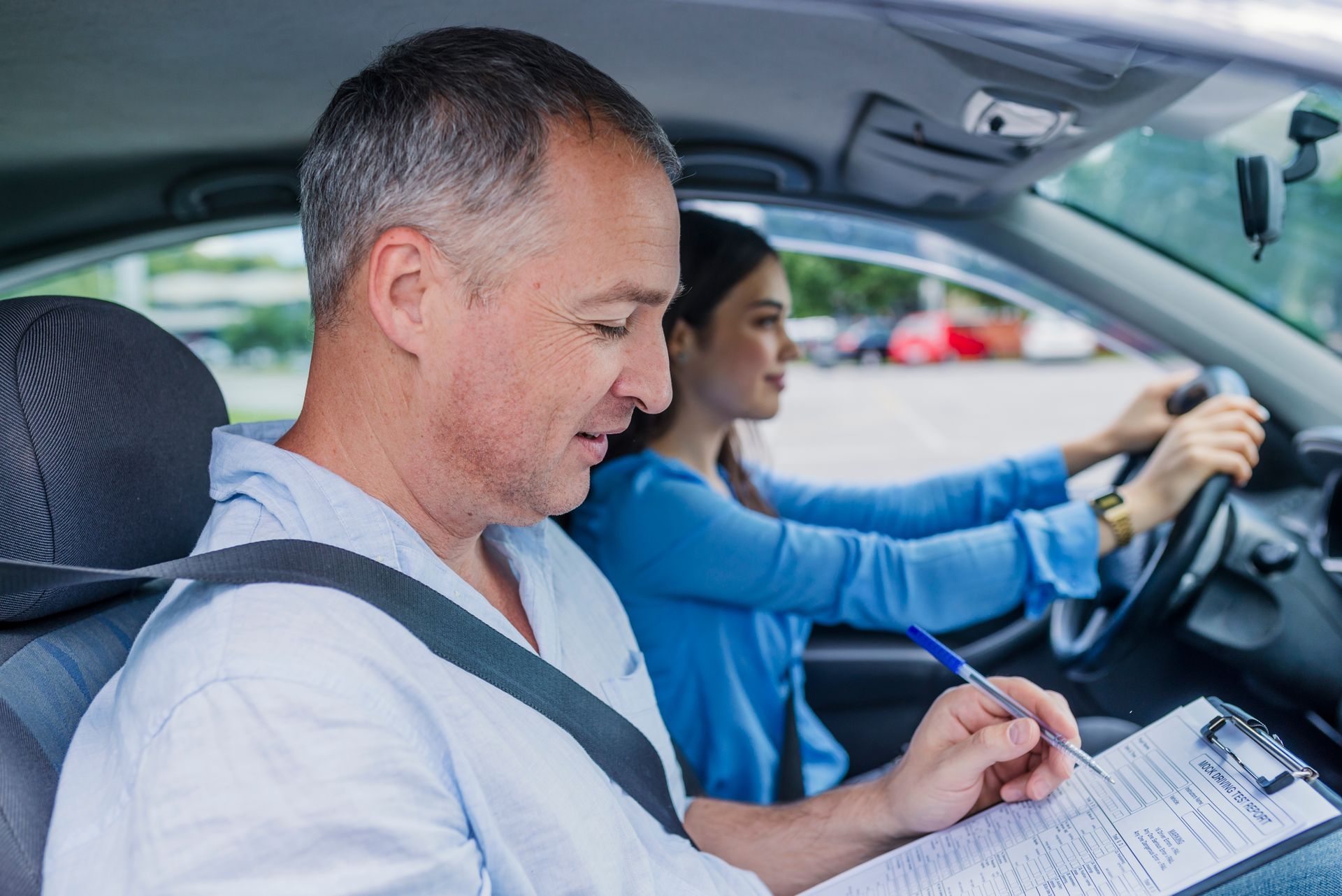 Driving instructor in car, writing on clipboard while student drives. Driving instructor in car, writing on clipboard while student drives.