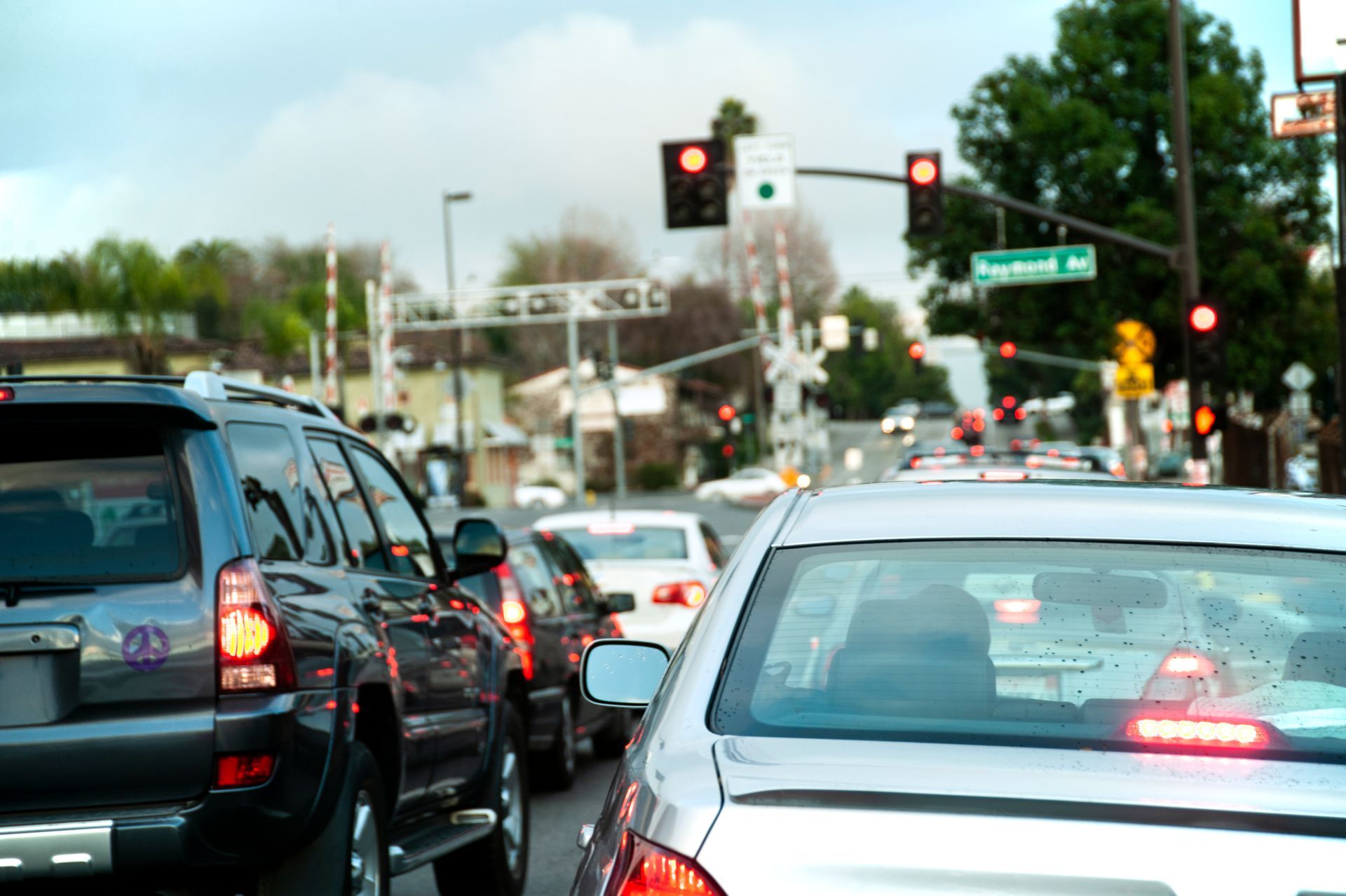 Cars stopped at a red traffic light, waiting in line on a street with a railroad crossing in the background.