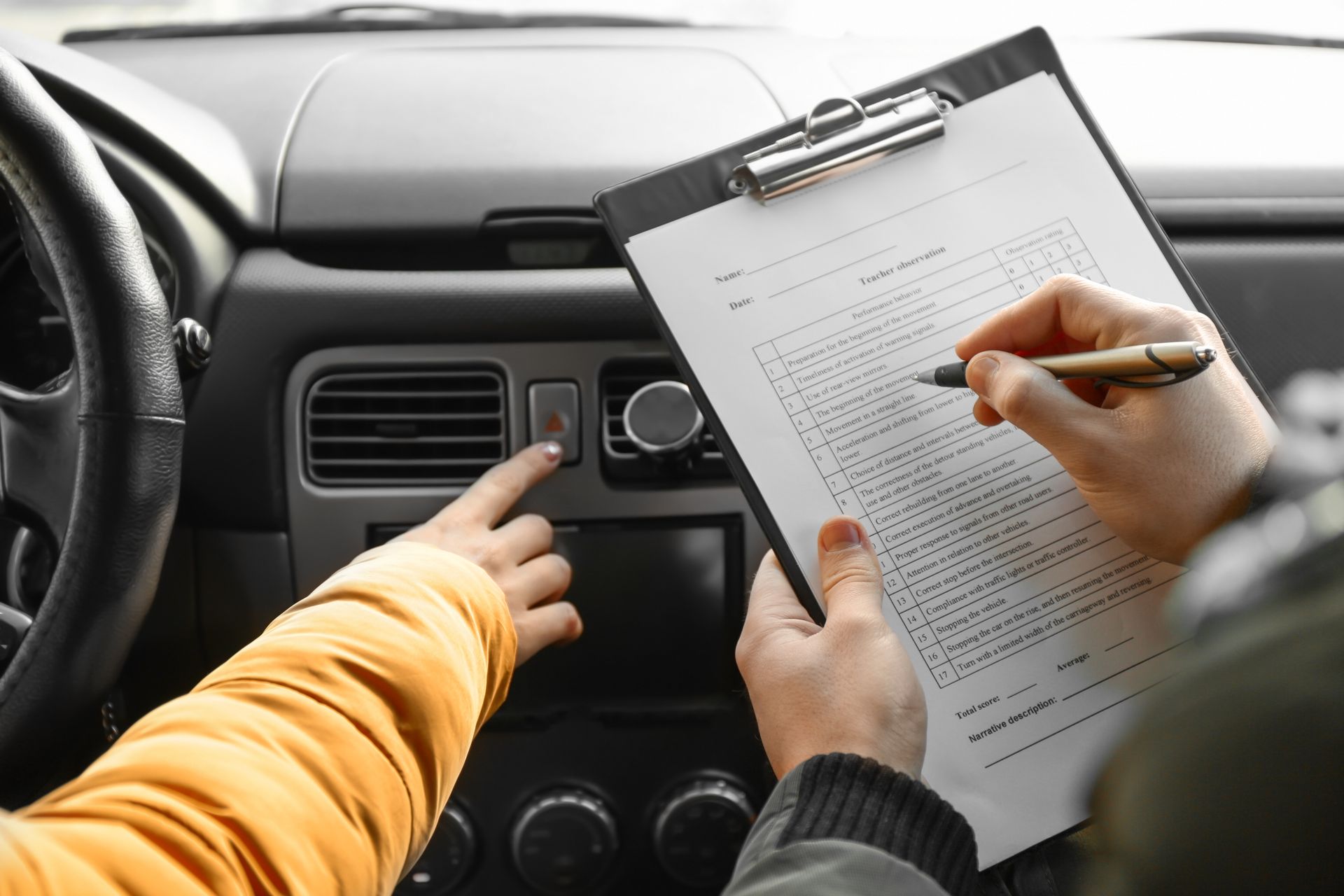 Person in car pointing at a button while another person marks a clipboard.