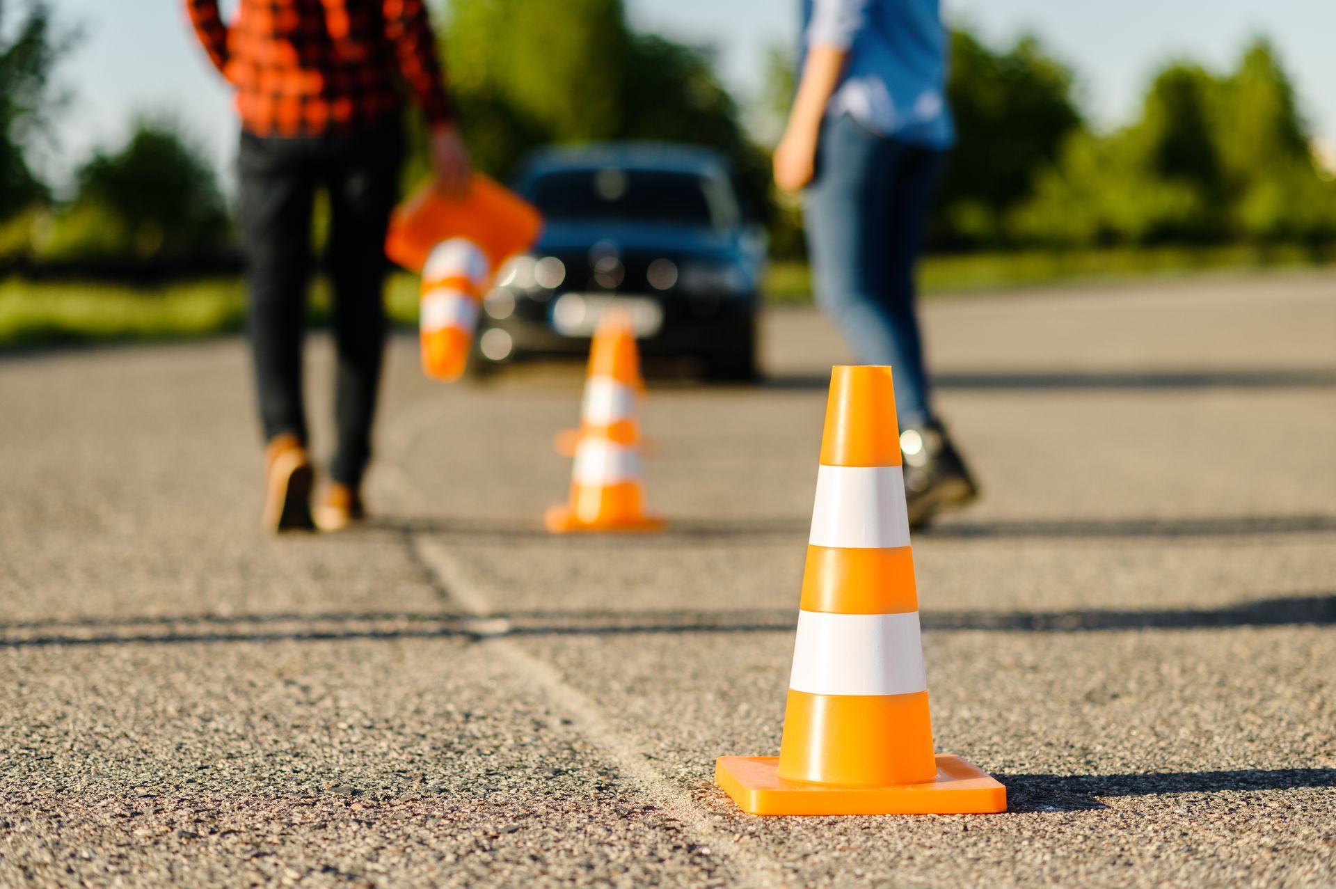 Traffic cones on asphalt with people and a car in the background.