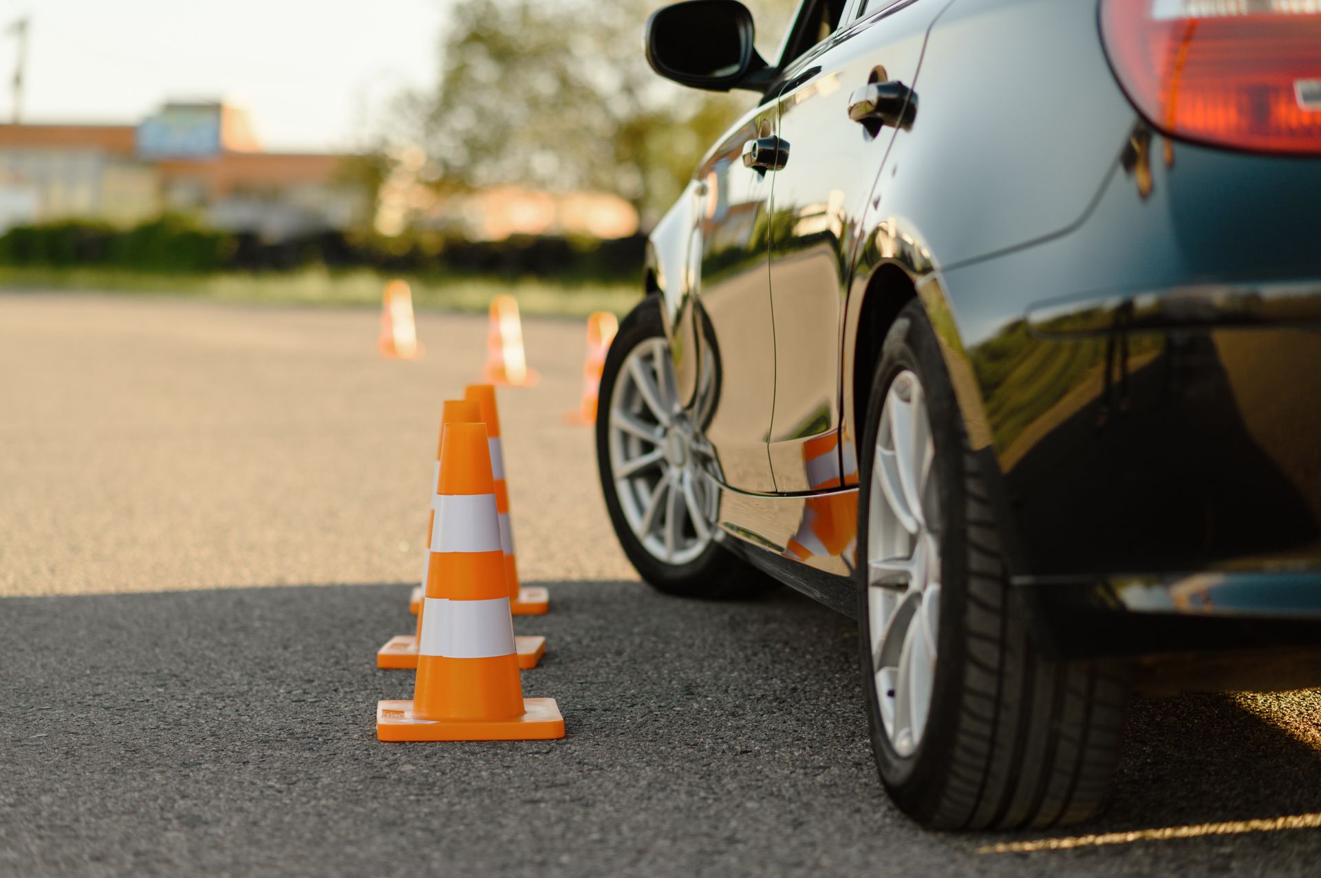 Black car parked next to orange traffic cones on an asphalt surface. Black car parked next to orange traffic cones on an asphalt surface.
