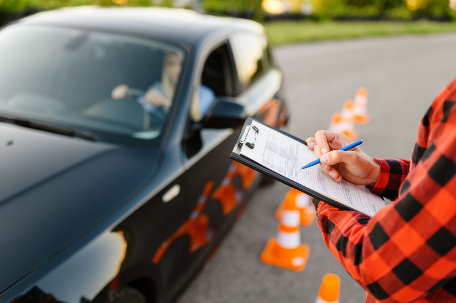 Driving instructor taking notes during a driving test. A black car sits next to orange cones. Driving instructor taking notes during a driving test. A black car sits next to orange cones.