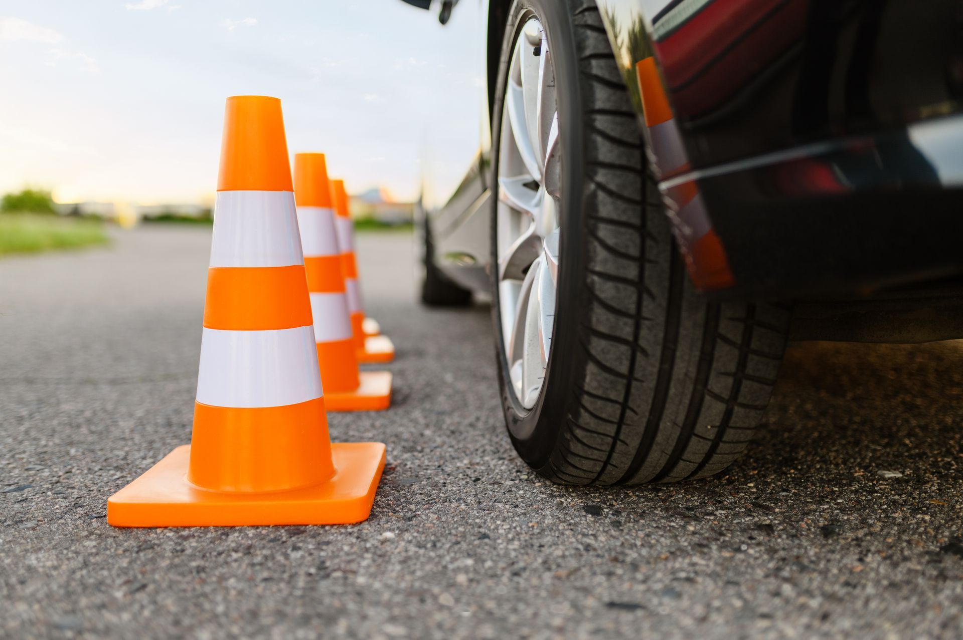 Orange traffic cones in a row, next to a car's tire on asphalt road. Orange traffic cones in a row, next to a car's tire on asphalt road.