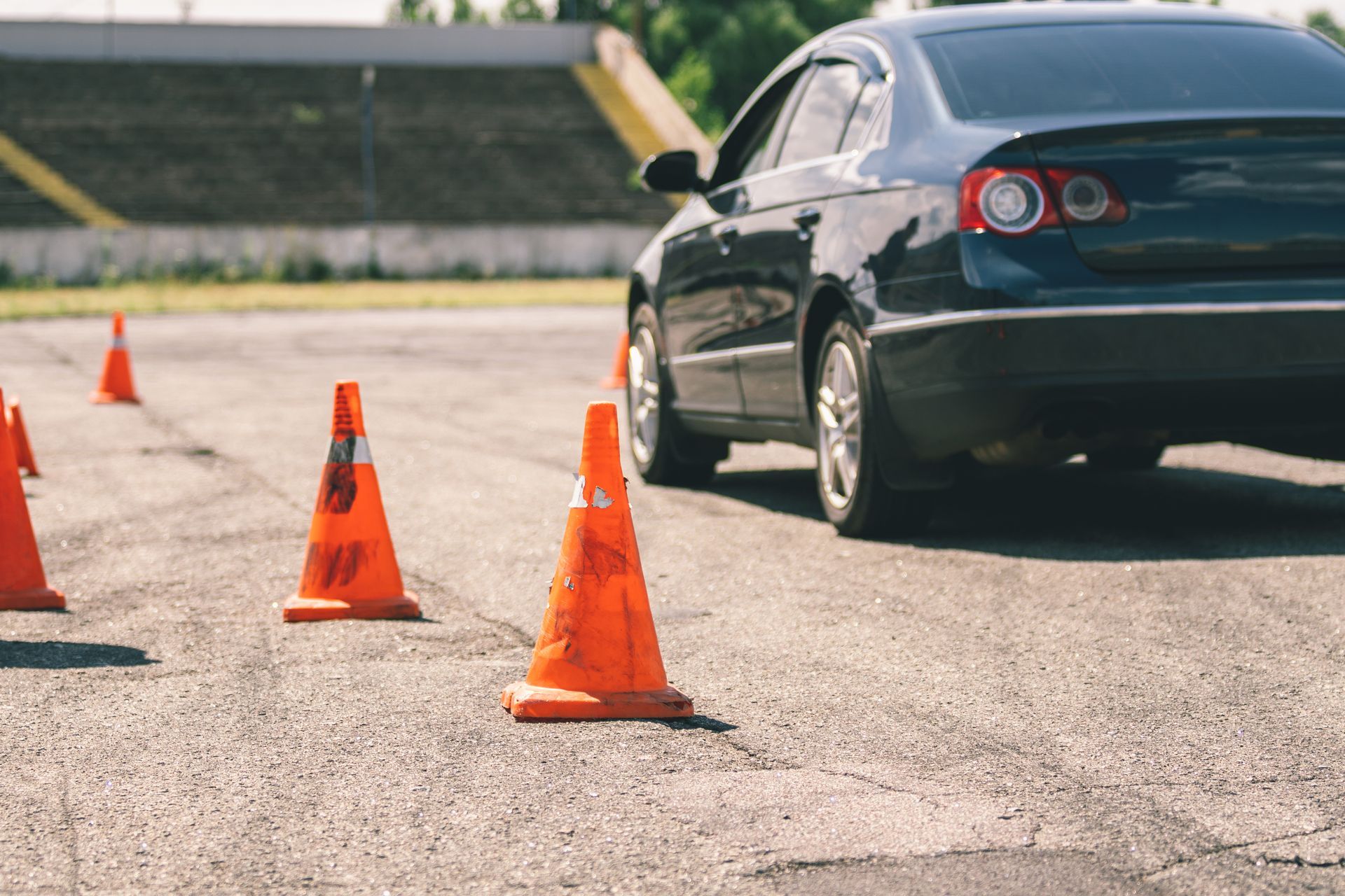 Dark blue sedan driving through orange traffic cones in a paved lot. Dark blue sedan driving through orange traffic cones in a paved lot.