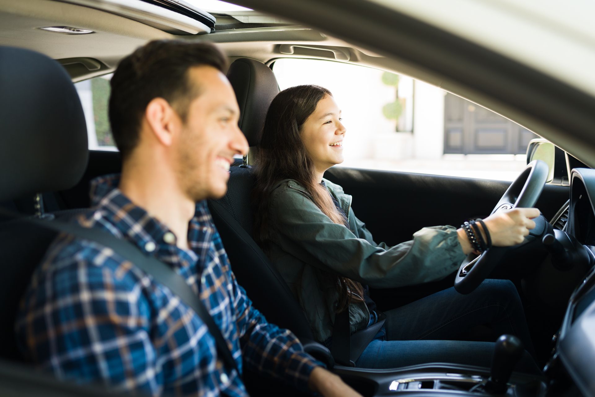 Man in passenger seat smiling, teen driver smiling, both wearing seatbelts in a car. Man in passenger seat smiling, teen driver smiling, both wearing seatbelts in a car.