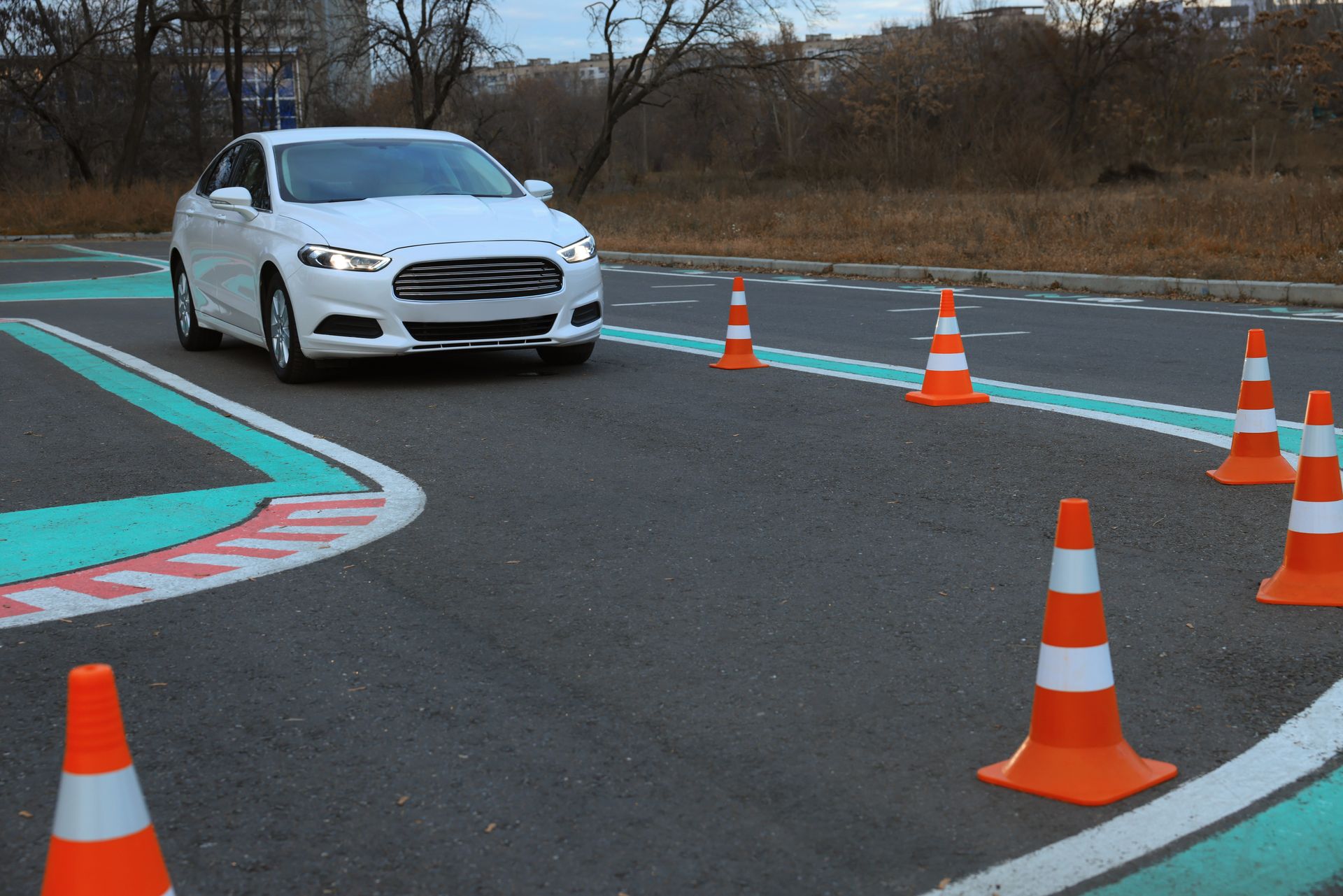 White car driving through driving test course with orange cones.