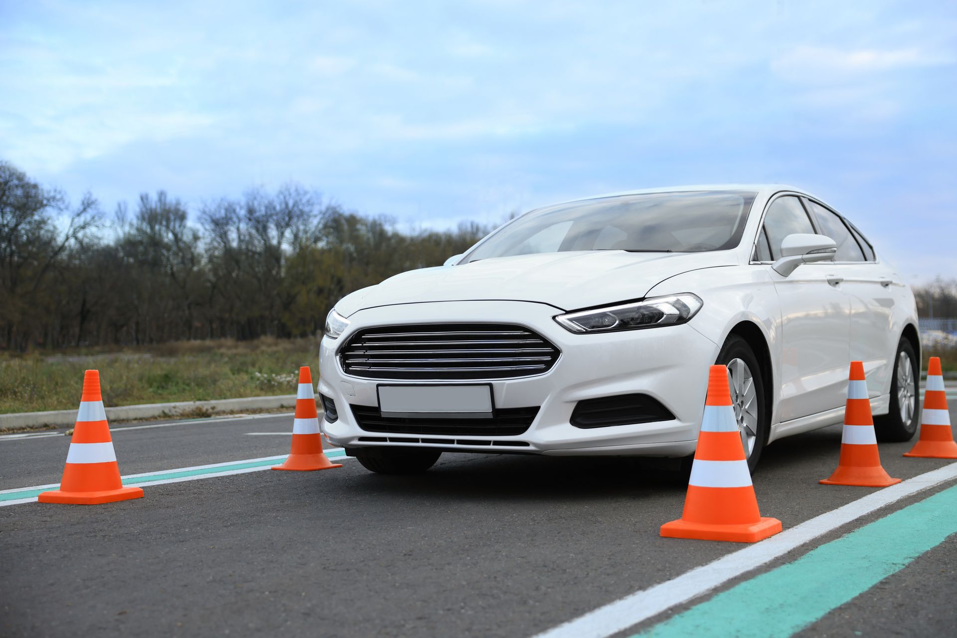 White car with orange cones on an asphalt driving course. Cloudy sky background. White car with orange cones on an asphalt driving course. Cloudy sky background.