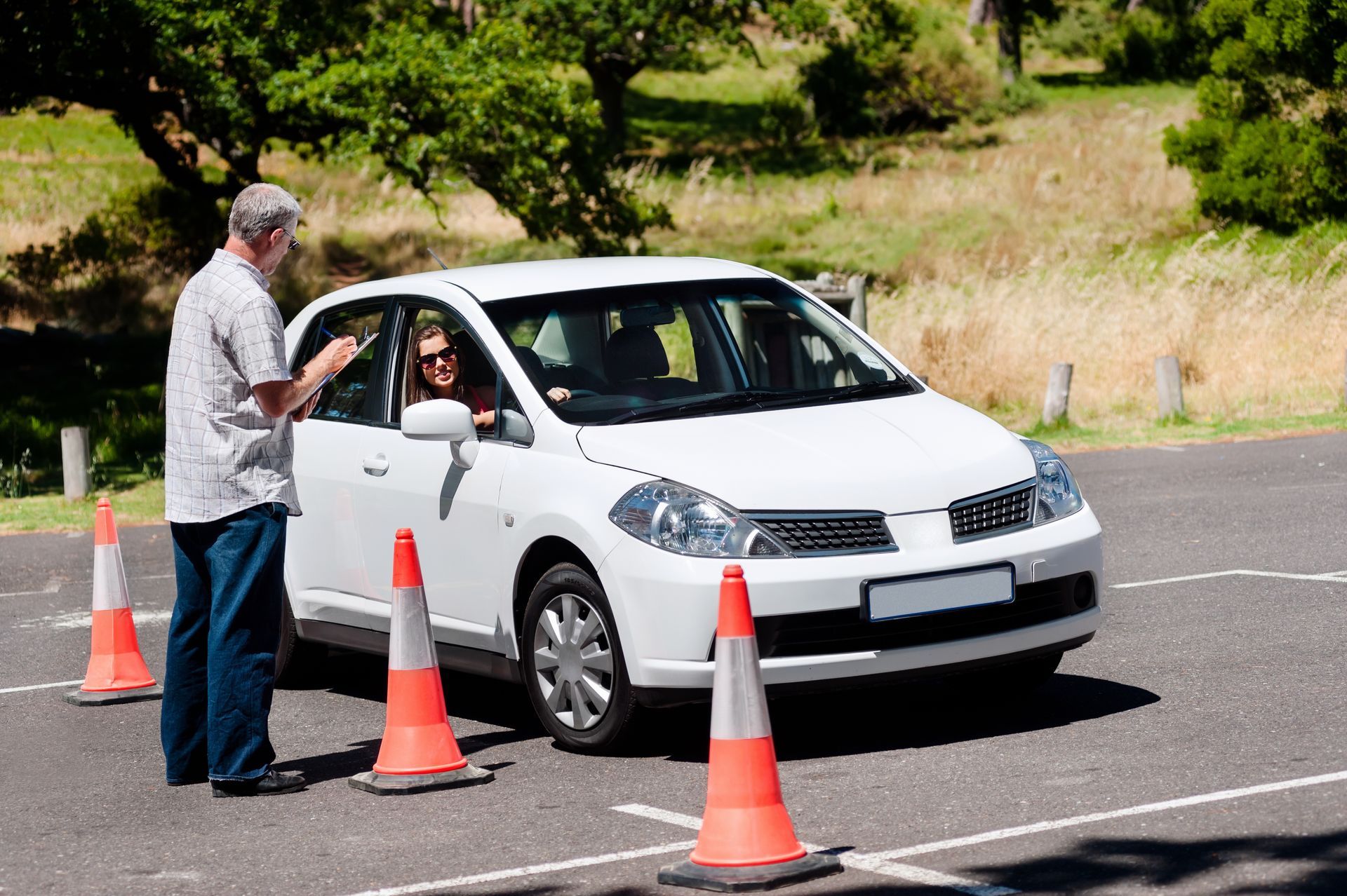 Man instructing a person driving a white car through orange cones. Sunny outdoor setting. Man instructing a person driving a white car through orange cones. Sunny outdoor setting.