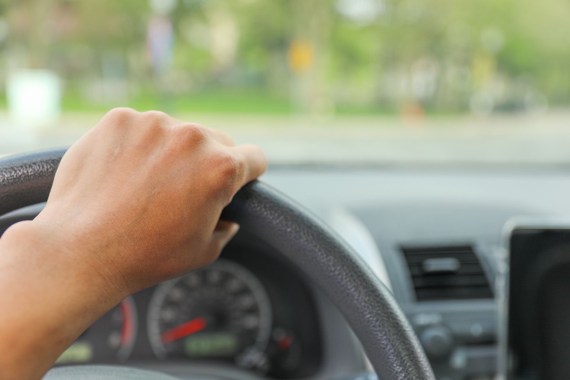 Hand gripping a black steering wheel inside a car, dashboard in view, driving. Hand gripping a black steering wheel inside a car, dashboard in view, driving.