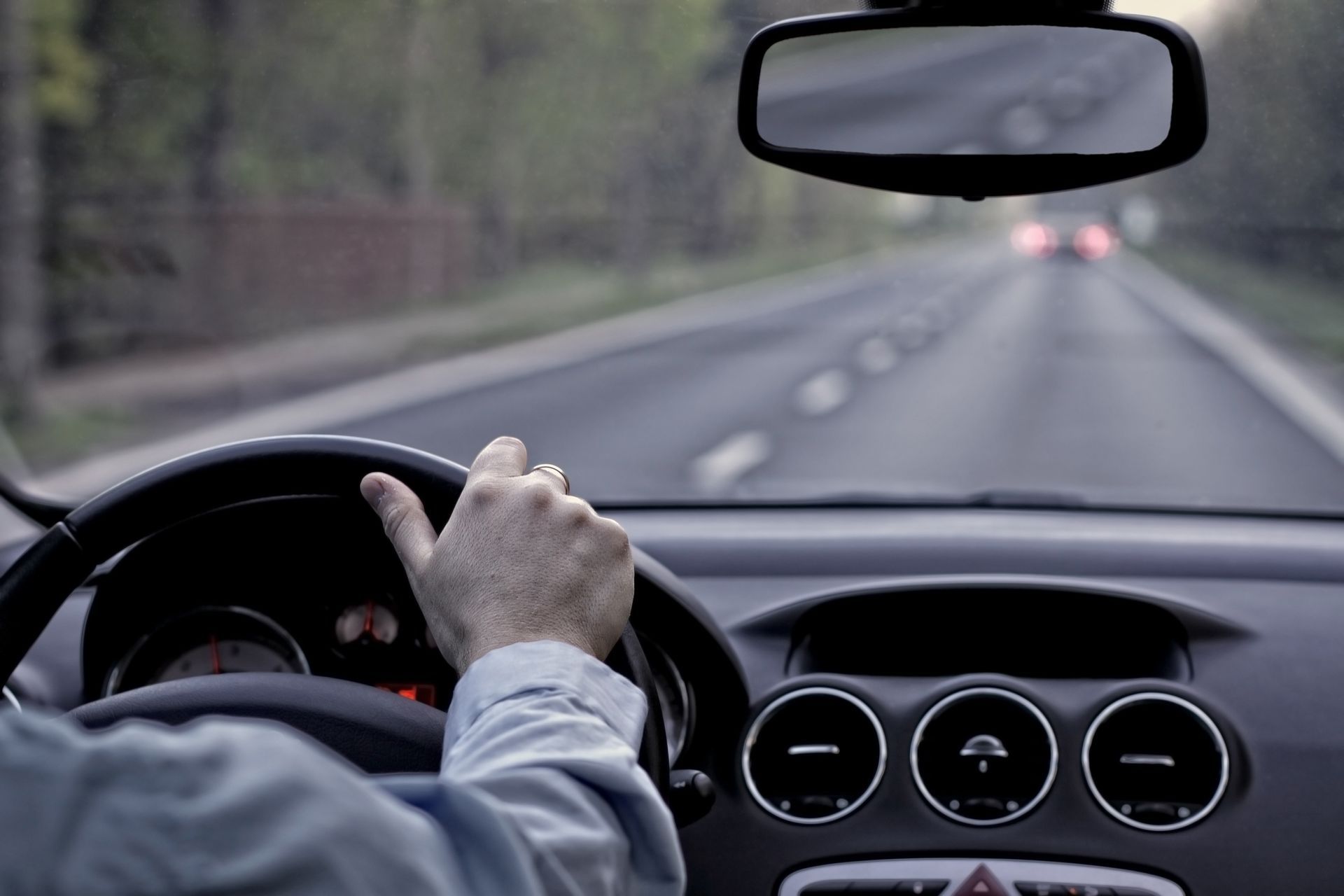 Driver's hand on steering wheel, view of road ahead through windshield.