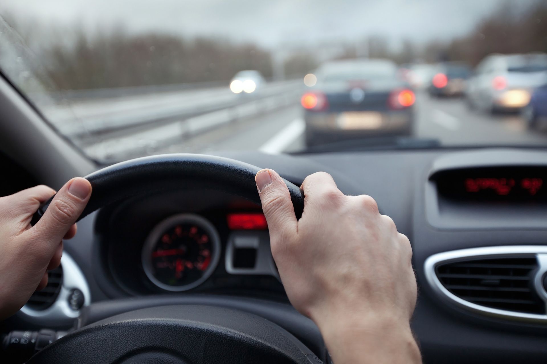Hands gripping a car steering wheel; driving on a highway with other vehicles.