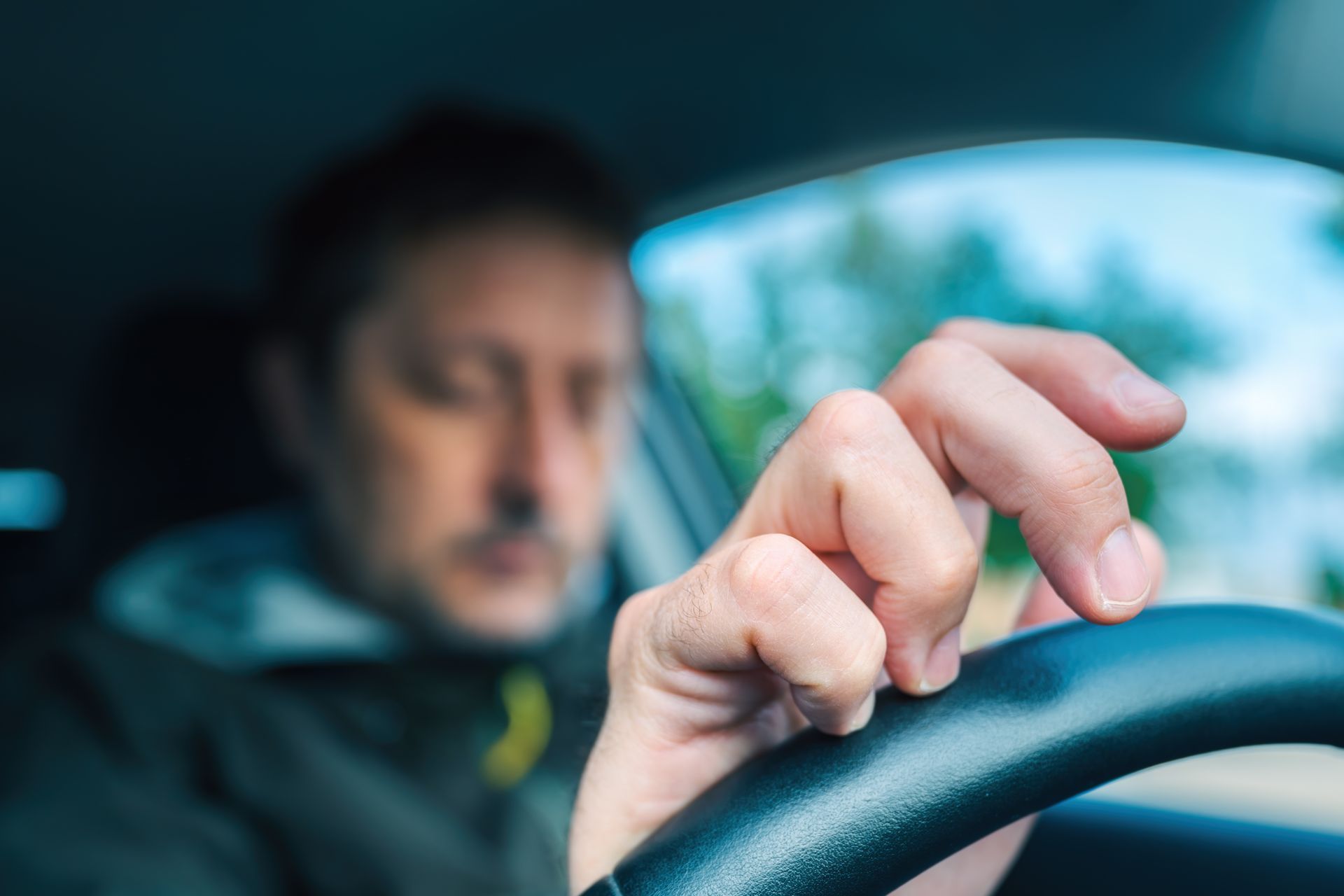 Nervous driver at the wheel, hand on the steering wheel inside a car, blurred background of trees. Nervous driver at the wheel, hand on the steering wheel inside a car, blurred background of trees.