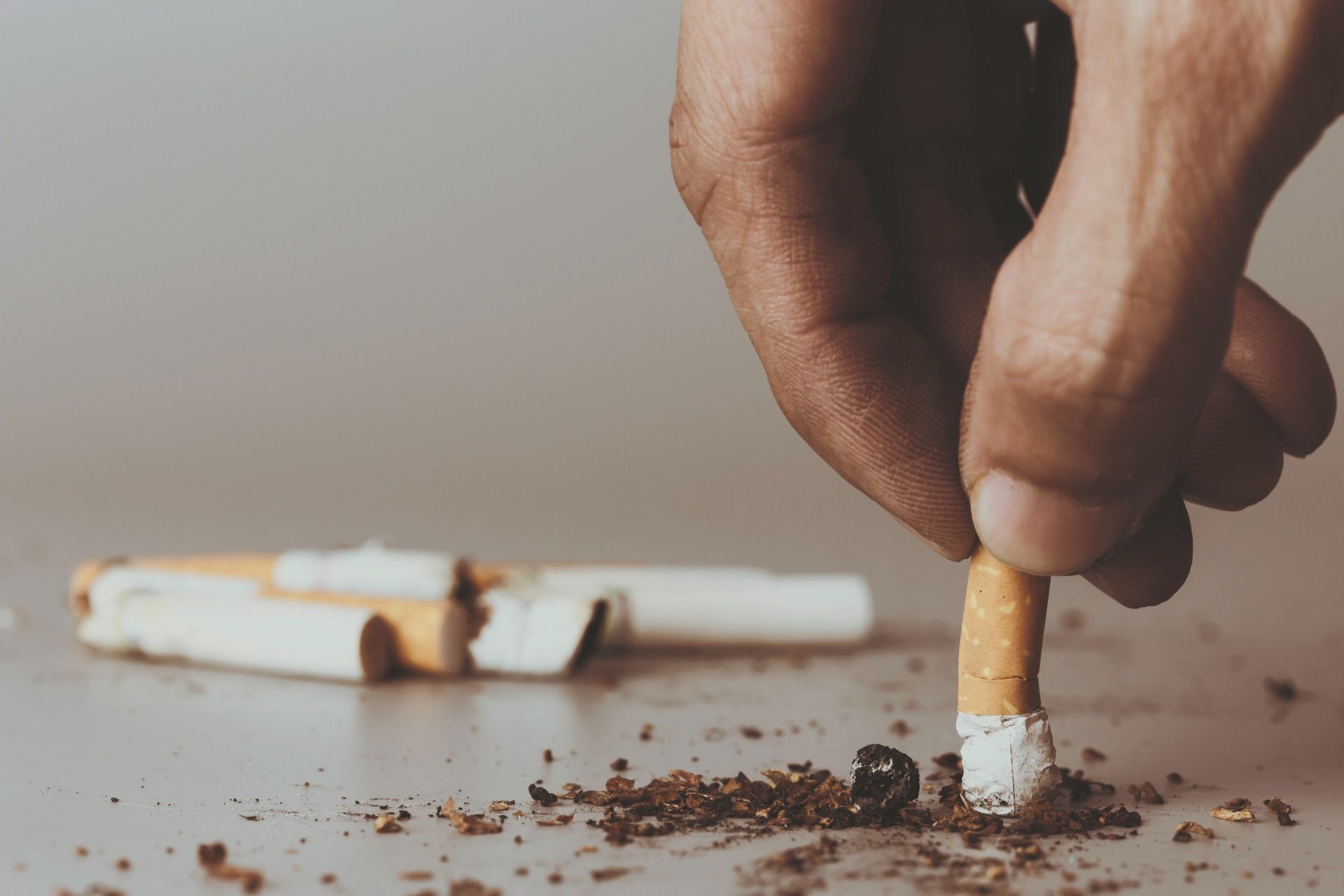 Hand placing a lit cigarette on the floor beside scattered ash and other cigarette butts