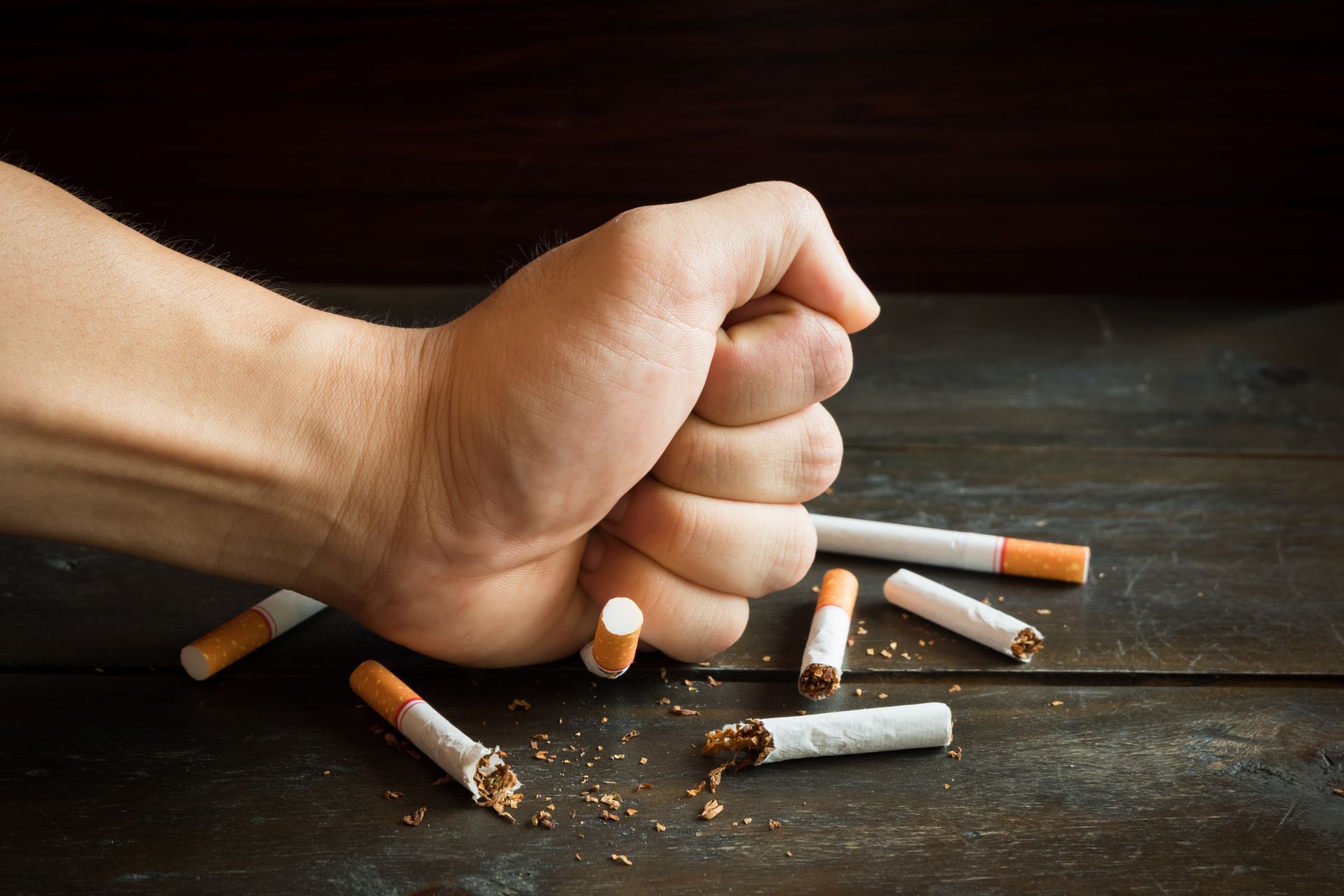 Clenched fist crushing several cigarettes on a dark surface, symbolizing quitting smoking