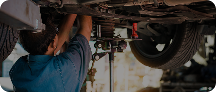 Mechanic working on a car from underneath, using tools in a garage. | GenAuto