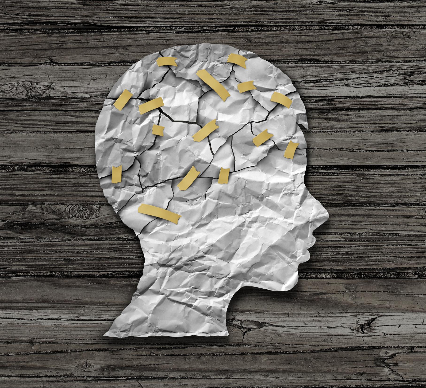 Silhouette of a head made of crumpled paper, cracked and patched with tape, on a wooden background.