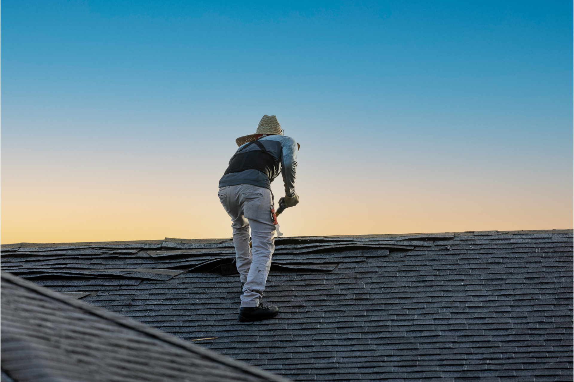 A man is standing on top of a roof with a hammer.