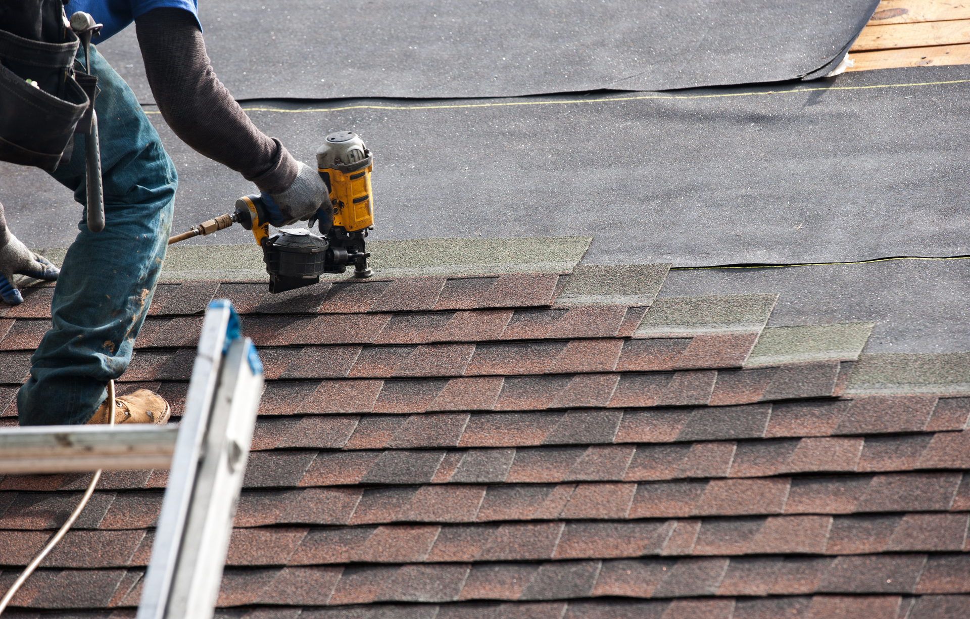 A man is standing on a ladder working on a roof in Bakersfield.