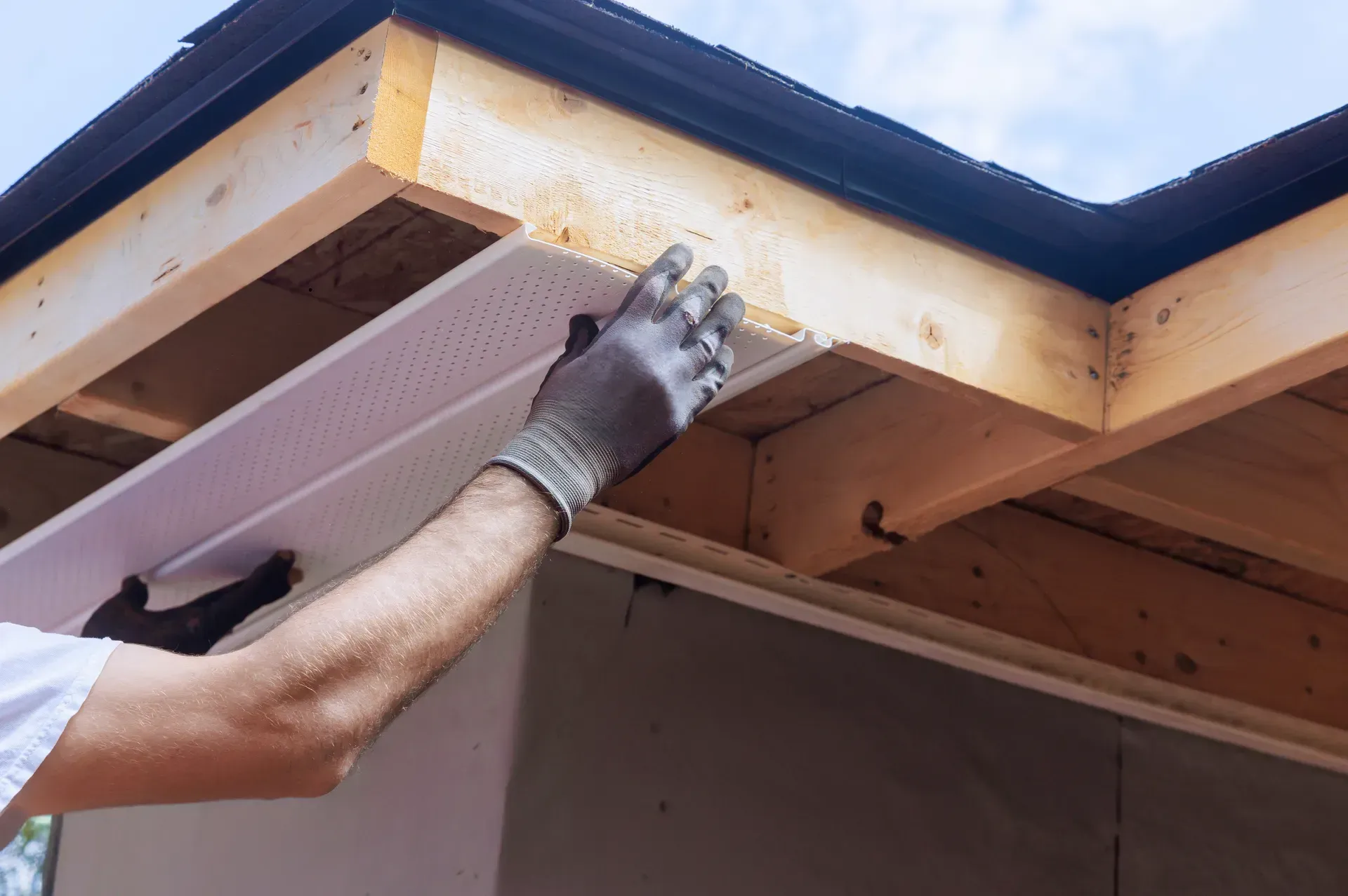 A man is installing soffit on the roof of a house.