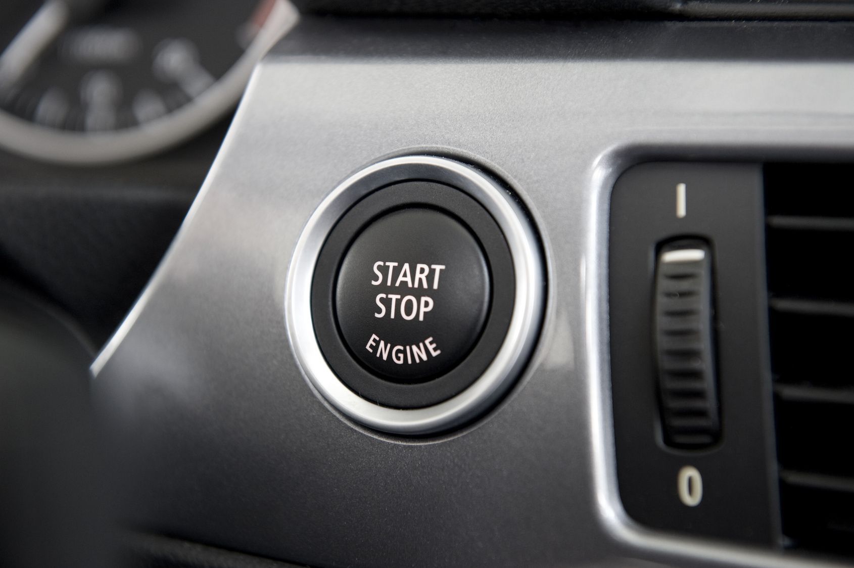 Close-up of a car's start/stop engine button with silver trim.