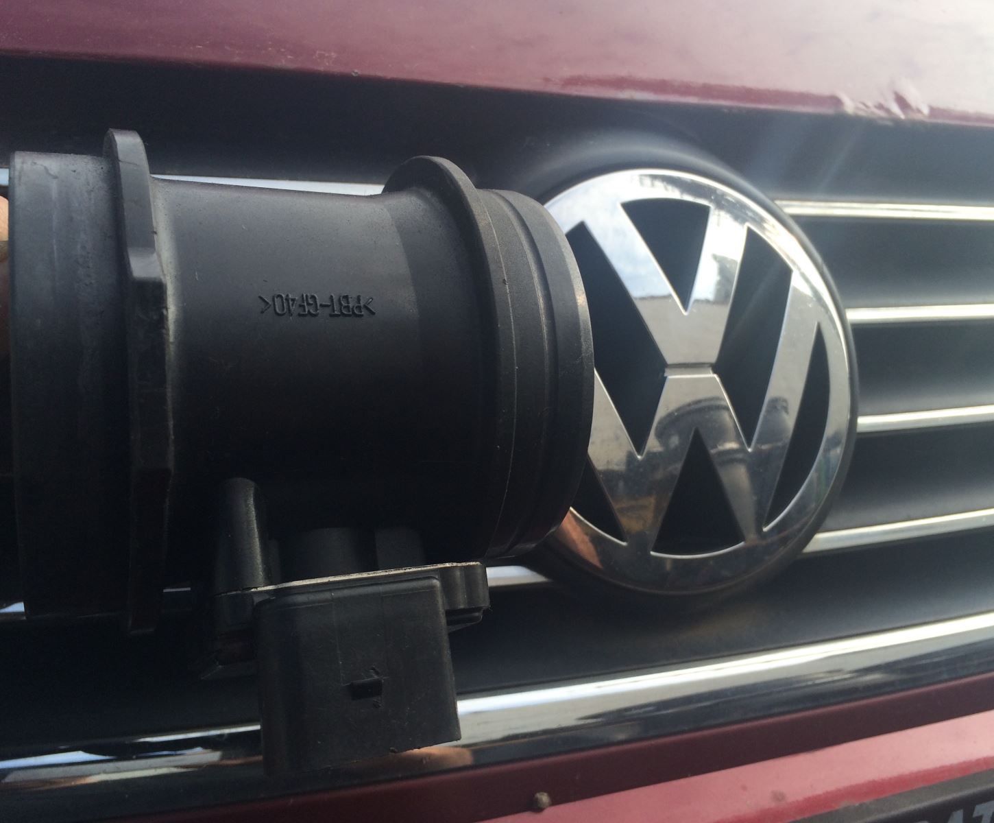 A black car part held in front of a Volkswagen emblem on a red car's grille.