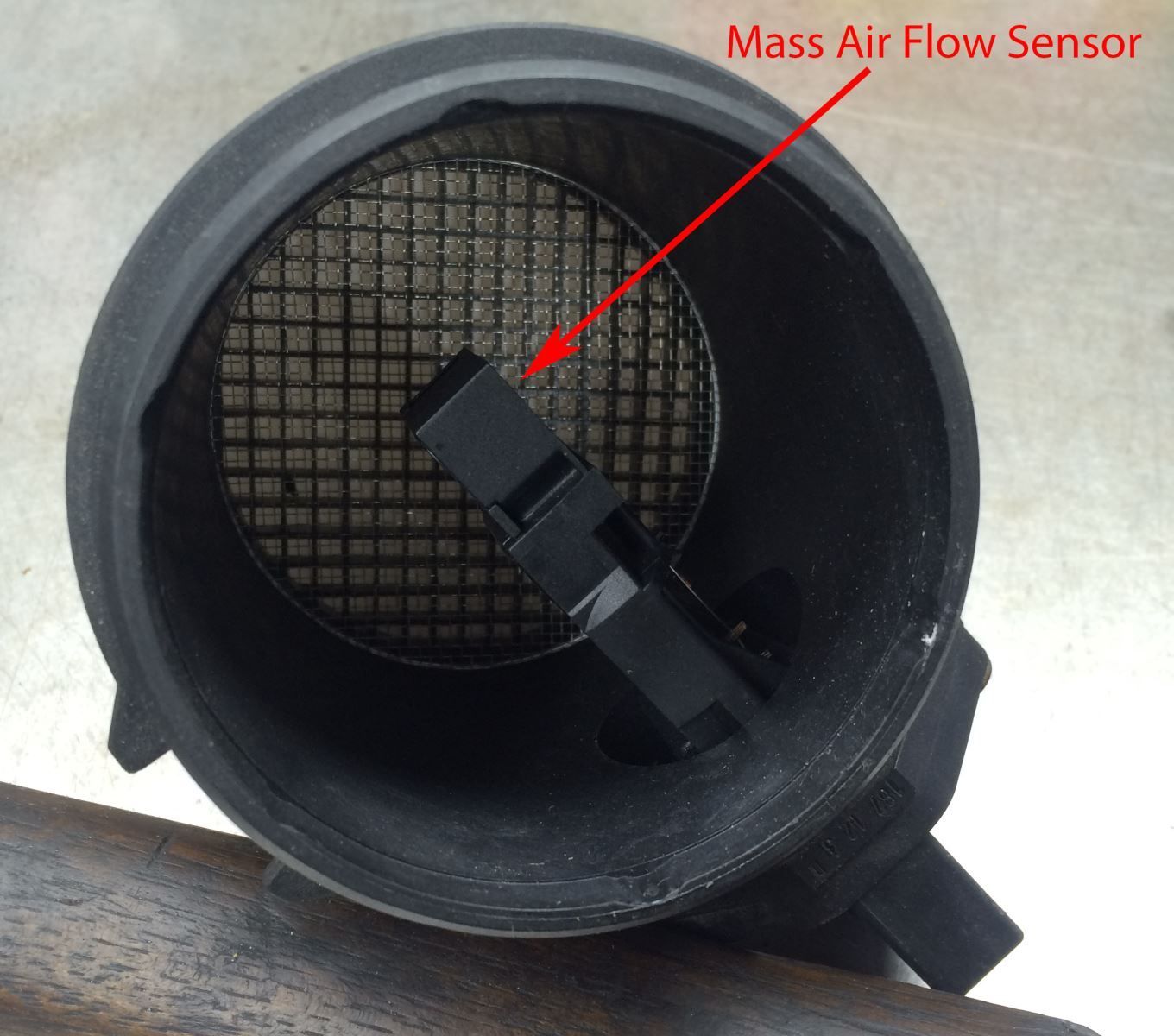 Mass air flow sensor inside a black tube, with a wire mesh and sensor pointed out with a red arrow.