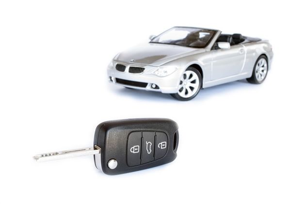 Silver convertible car with a black car key lying in front of it.