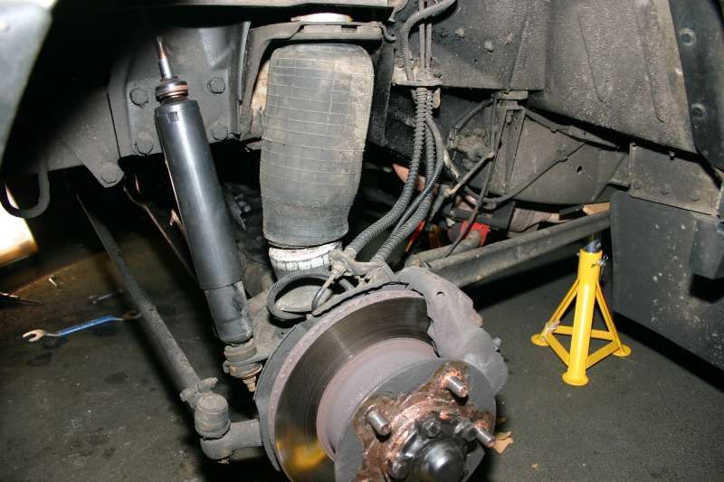 Car's rear suspension, showing an air spring, shock absorber, brake rotor, and jack stand.