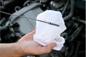 Hand holding an oil dipstick wiped with a white cloth, checking the oil level in a car engine.