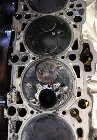 Engine cylinder head with burnt valves, showing internal damage and carbon buildup.