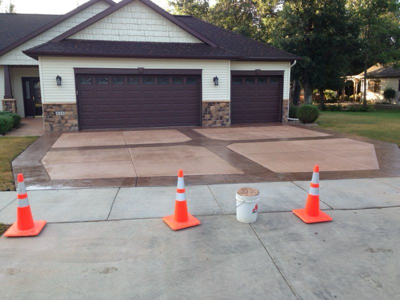New suburban house with dark siding, white garage, and a long concrete driveway under construction
