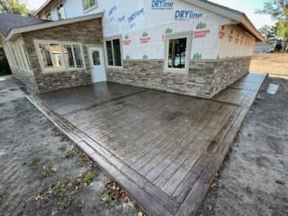 Concrete being poured from a truck onto a road construction site, with a worker’s gloved hand visible.