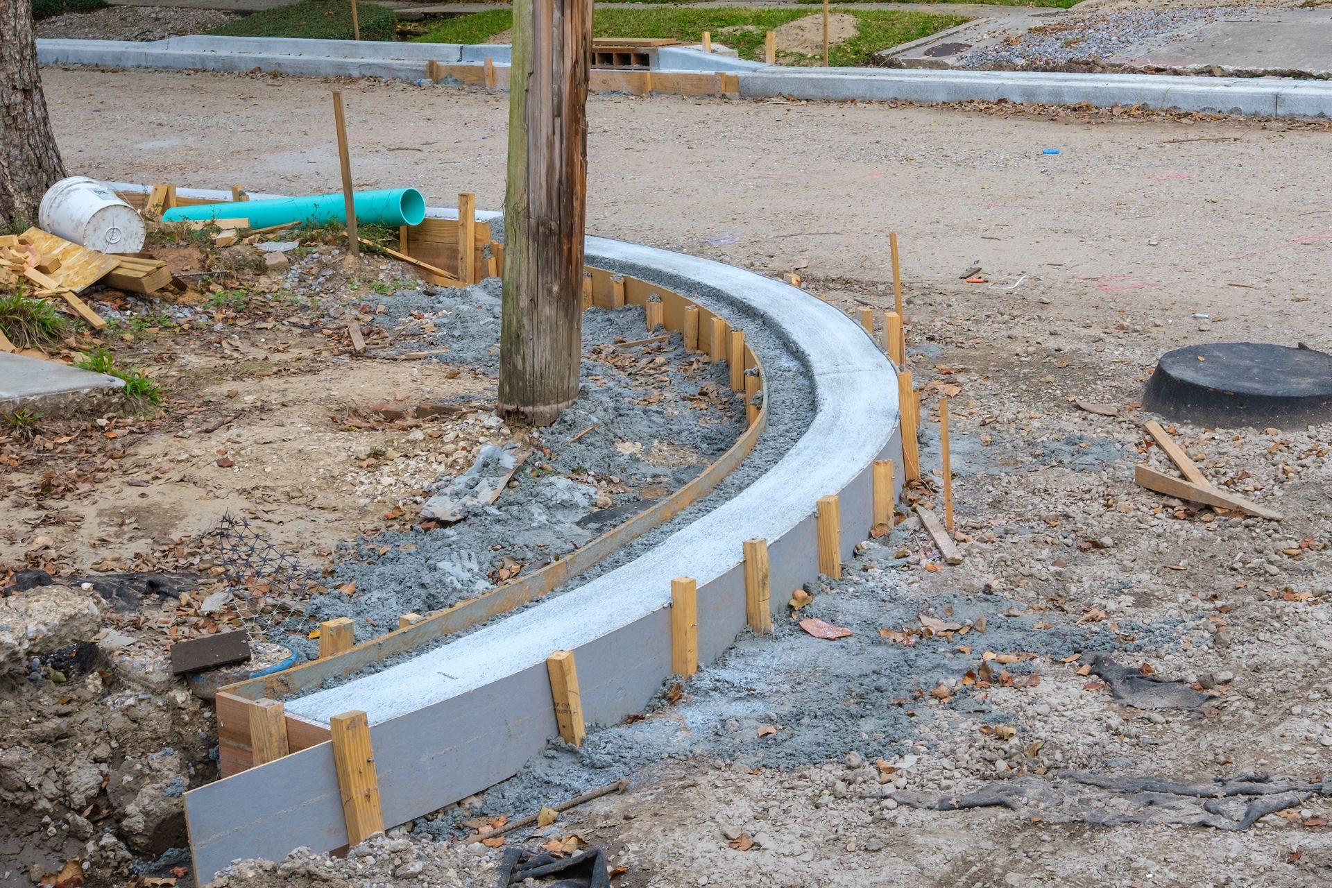 Curved concrete curb under construction beside a wooden post and gravel roadside