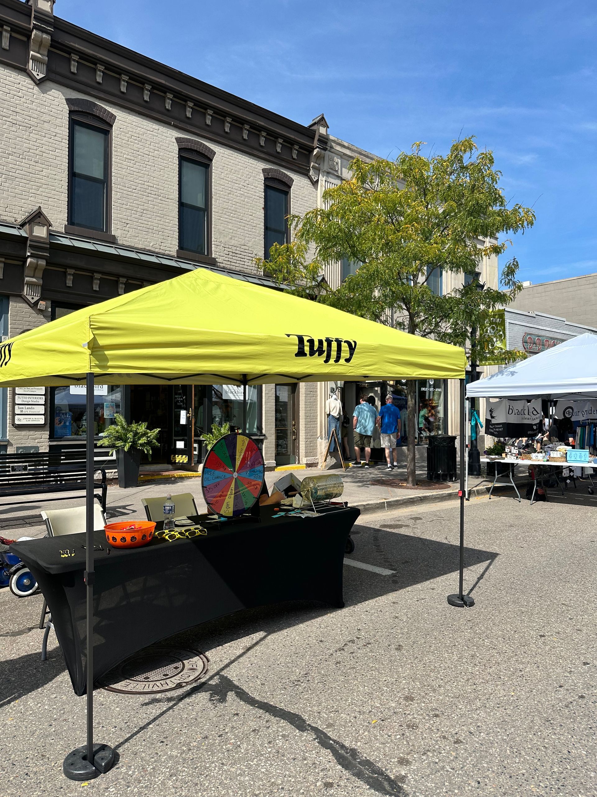 Yellow tent set up on a brick-paved street with people and storefronts.