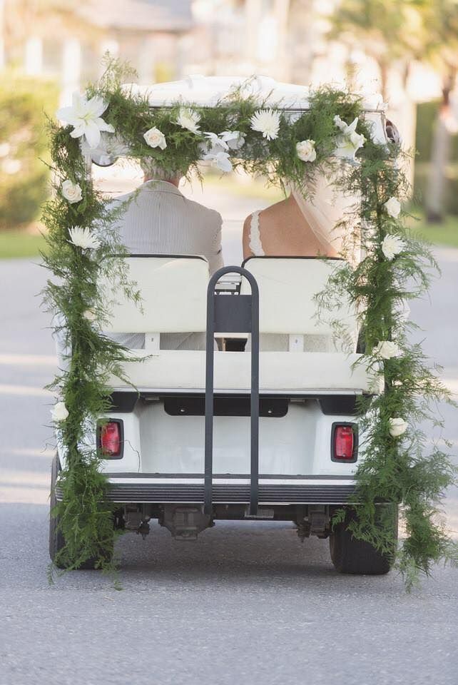 bride and groom riding on golf cart with greenery