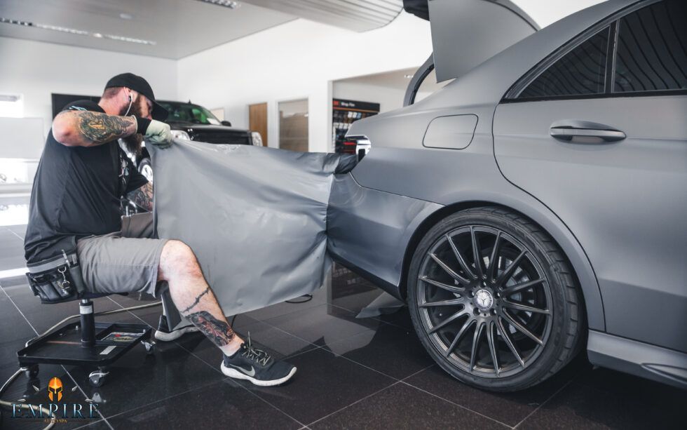 A man is wrapping a car with a cloth in a showroom.