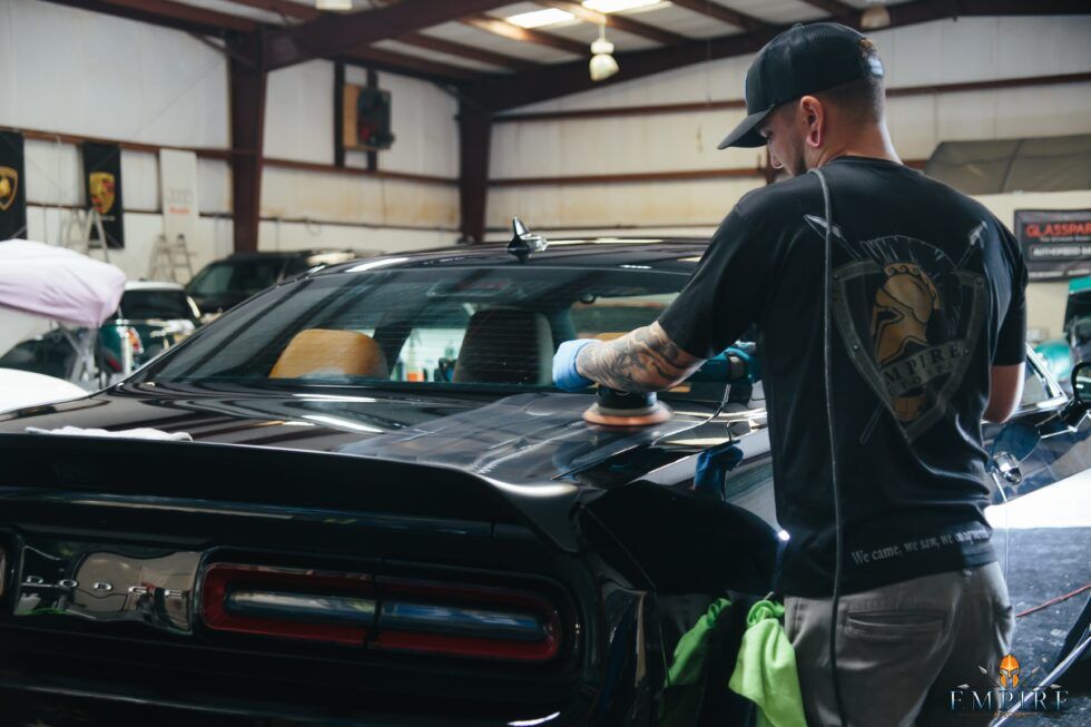 A man is polishing the hood of a car in a garage.