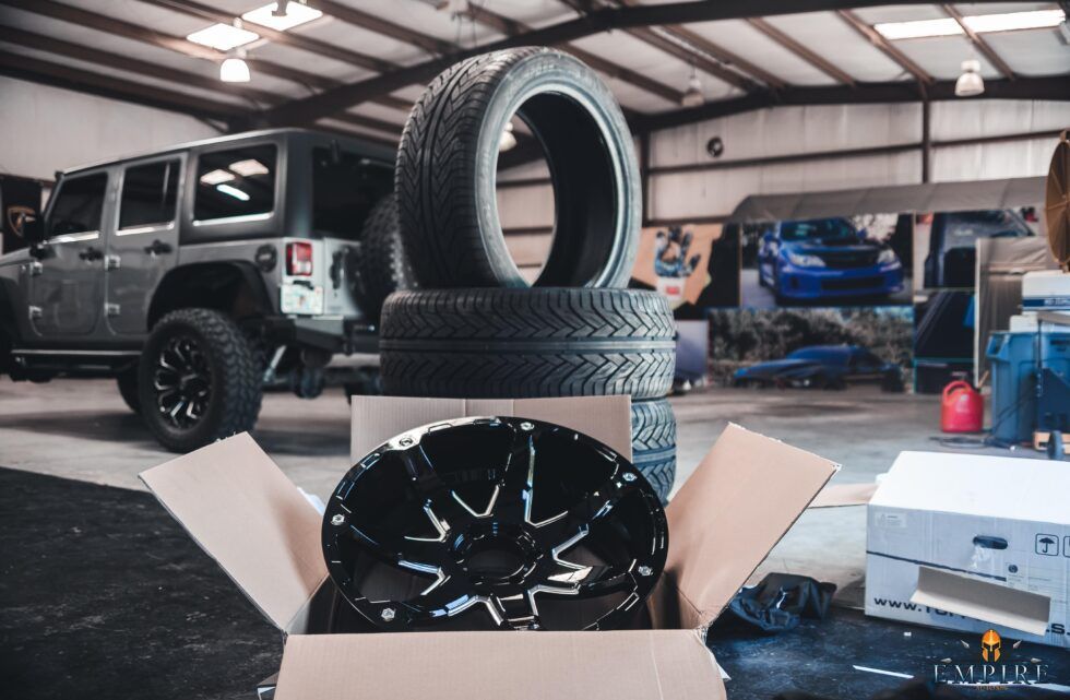 A jeep is parked in a garage next to a box of tires and wheels.