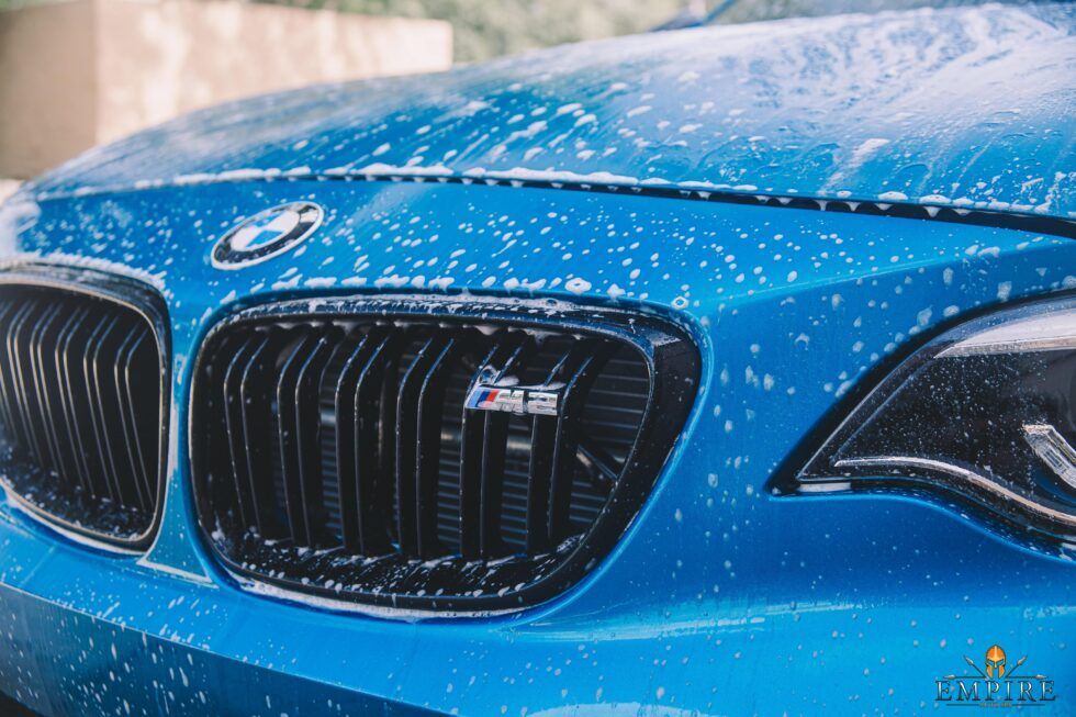 The front of a blue bmw m2 is covered in foam.