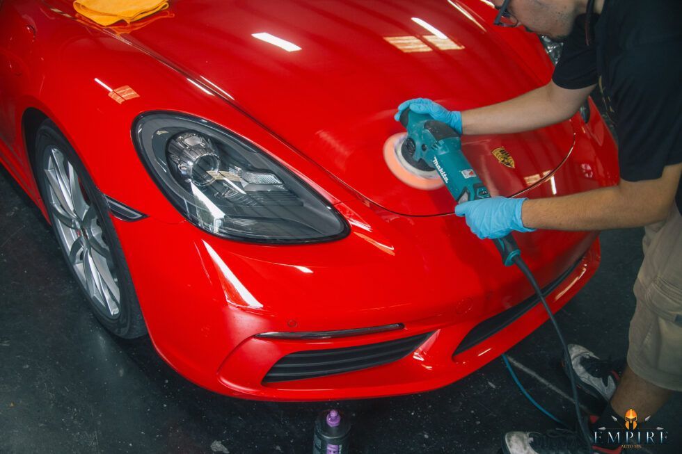 A man is polishing a red car with a machine