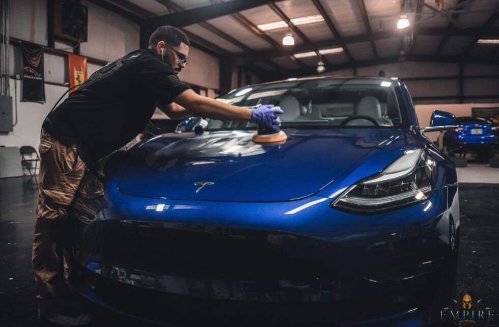 A man is polishing a blue tesla model 3 in a garage.