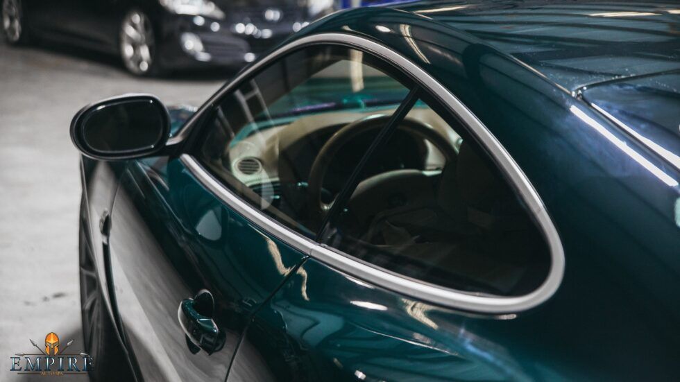 A green sports car is parked in a garage next to another car.