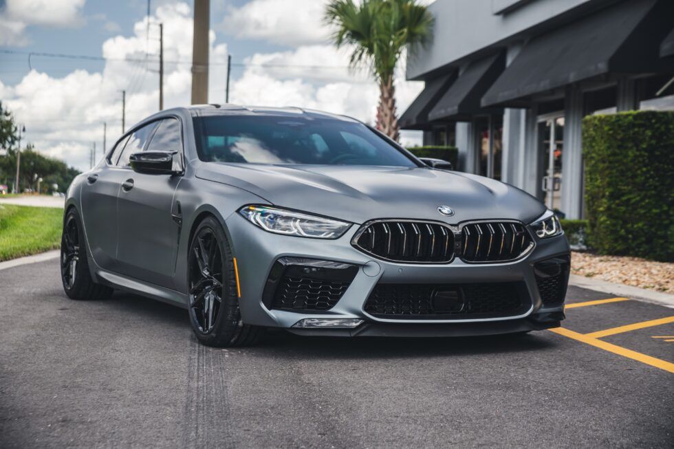 A bmw m8 is parked in a parking lot in front of a building.