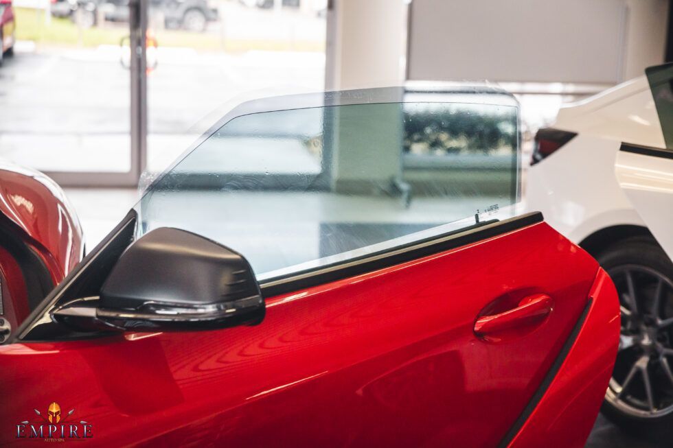 A red sports car is parked in a showroom with its door open.