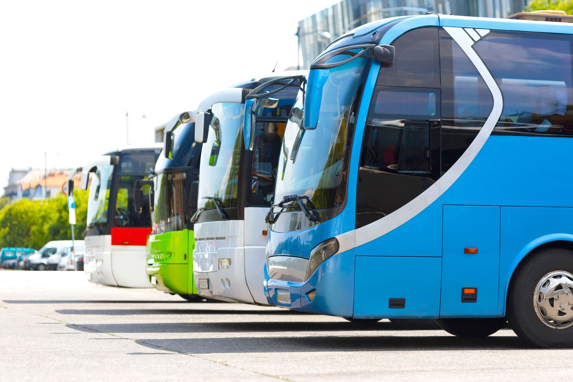 A row of parked tour buses on a street with buildings and trees in the background.