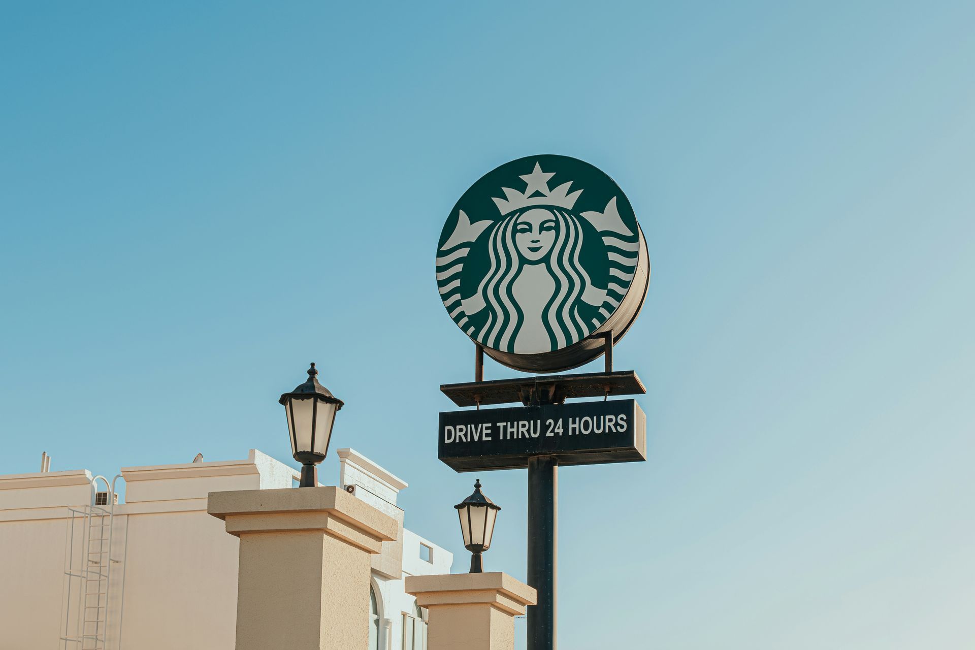A starbucks sign is sitting on top of a pole in front of a building.