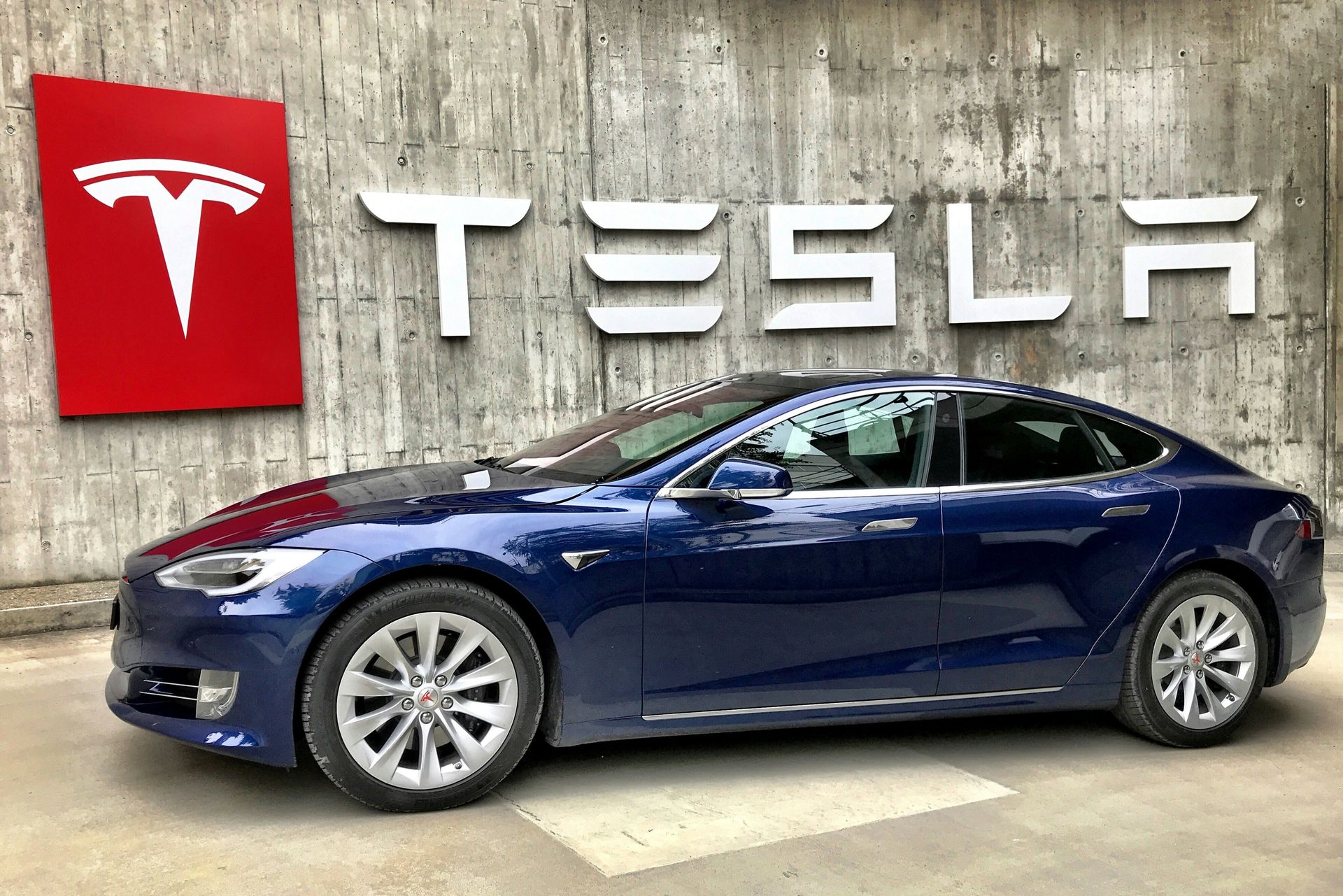 A blue tesla model s is parked in front of a tesla sign.