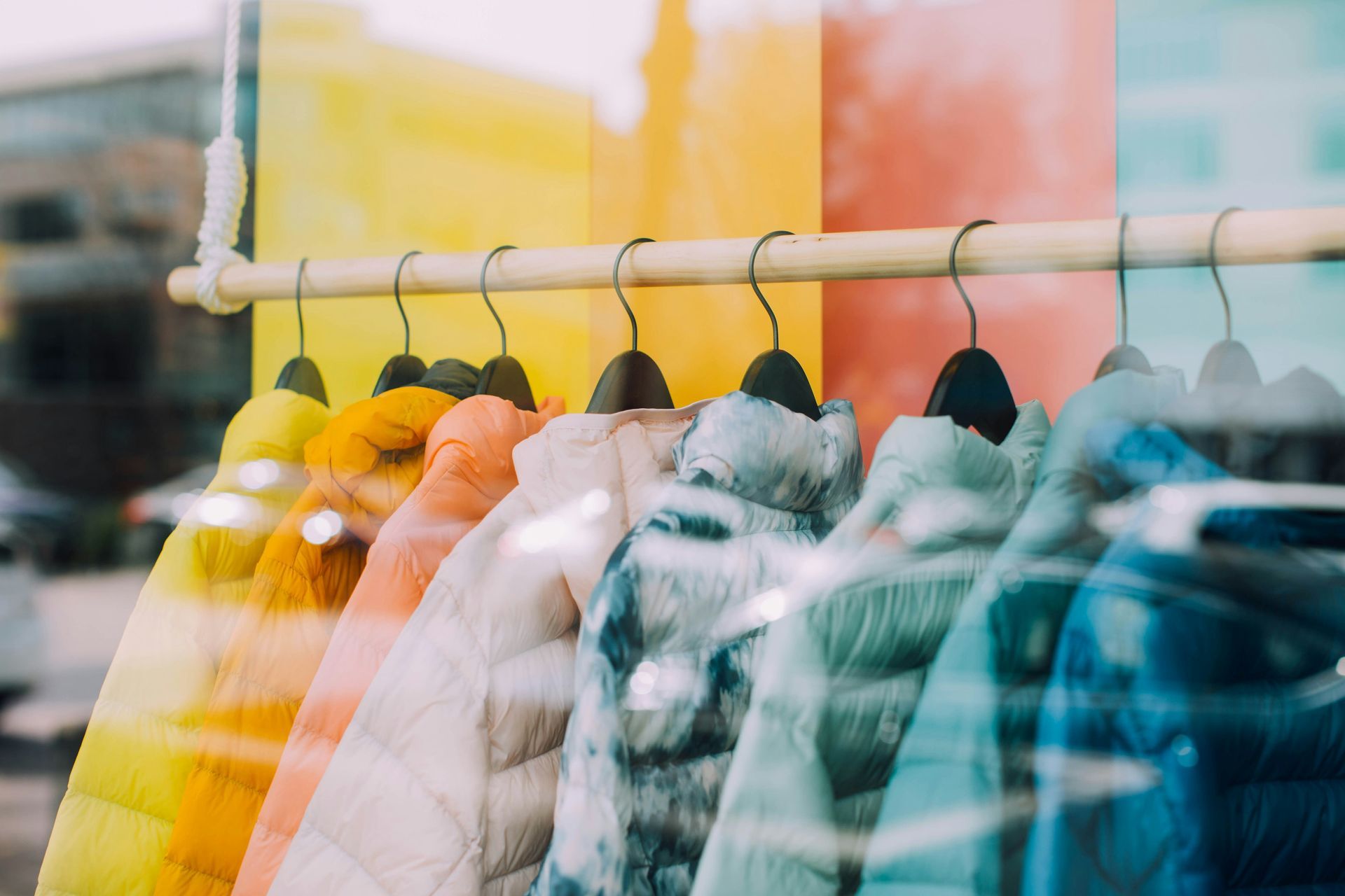 A row of colorful jackets hanging on a rack in a store window.