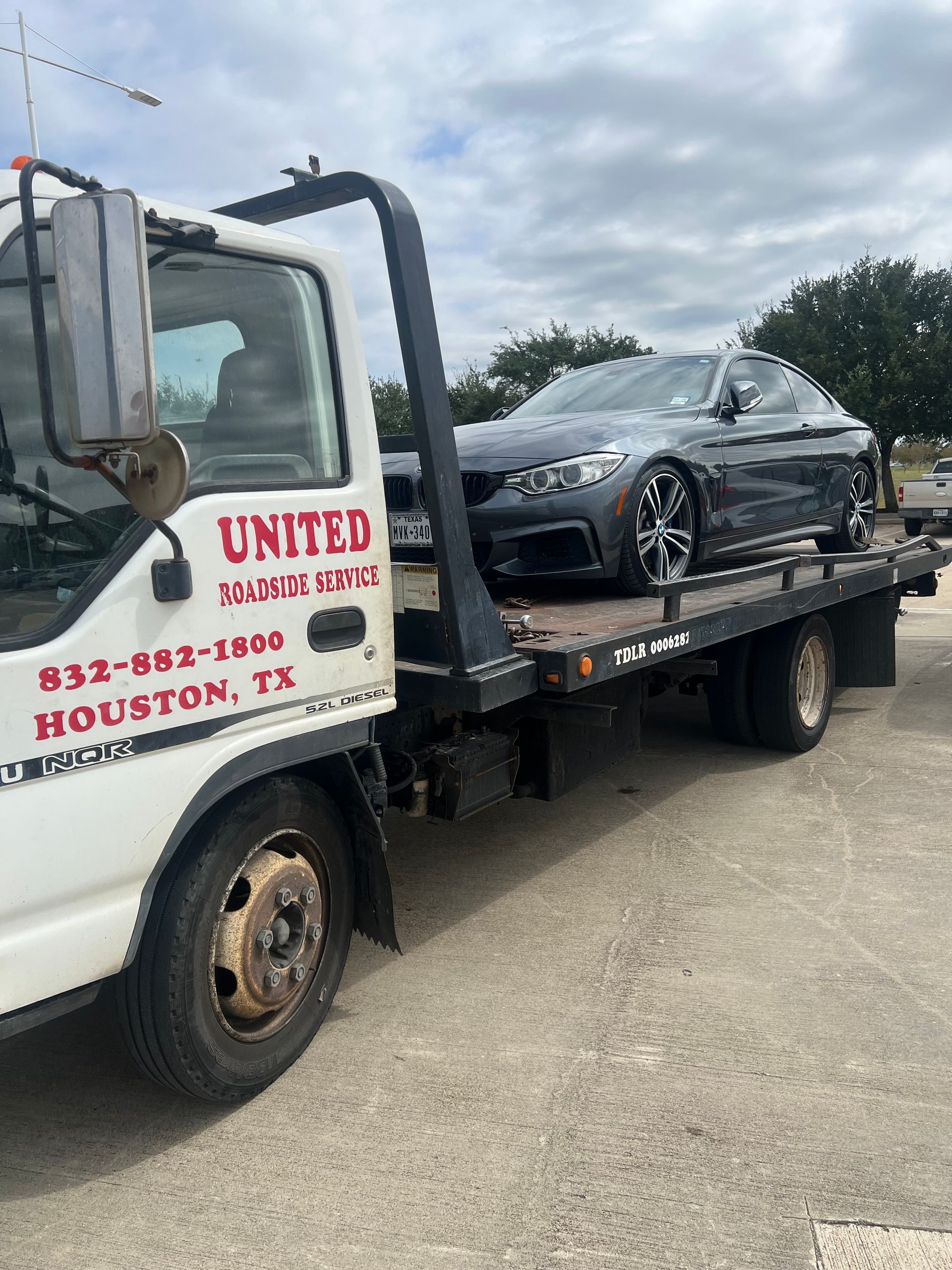 Tow truck hauling a damaged black car on a flatbed in a parking lot